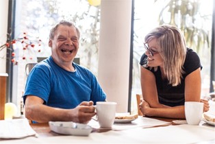 Image of a disability support worker sharing a laugh with a participant over coffee